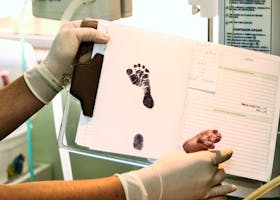 Healthcare professional handling newborn's footprint documentation in a hospital room.